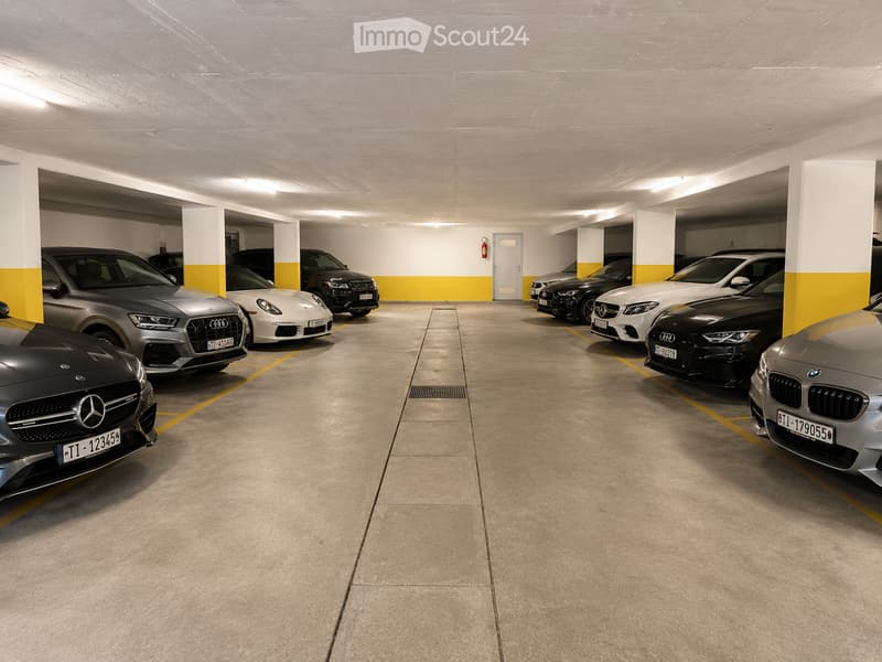 Underground parking area with multiple parked cars, concrete floors, white and yellow walls, and a fire extinguisher on the wall.