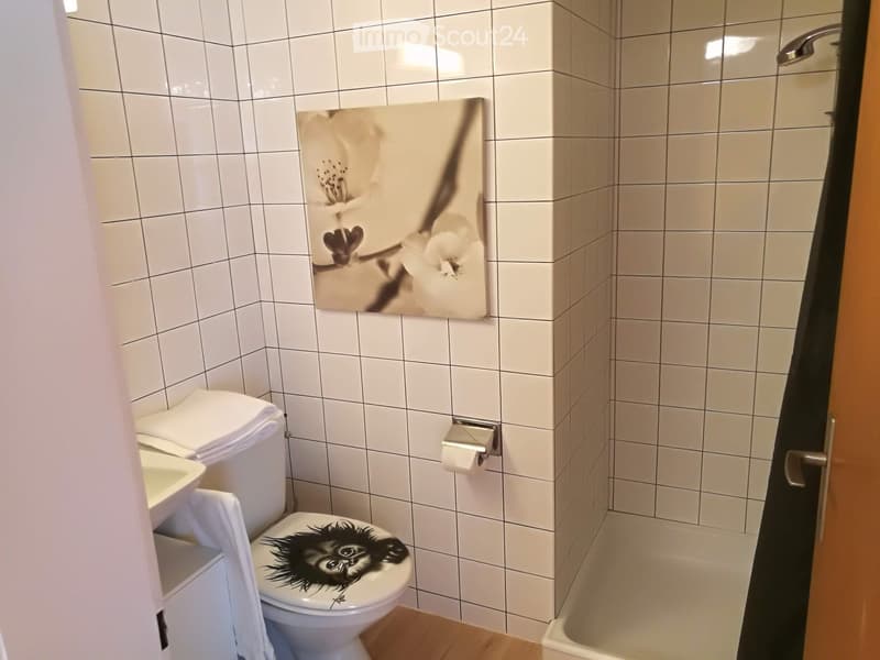 White tiled bathroom with a toilet, sink, bathtub, and a decorative picture of a flower on the wall.
