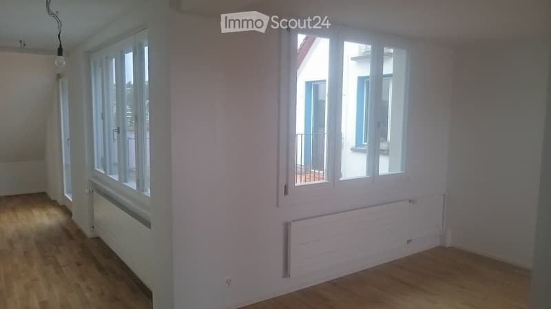 Empty room with wooden flooring, white walls, large windows, and radiators. No furniture or equipment present.