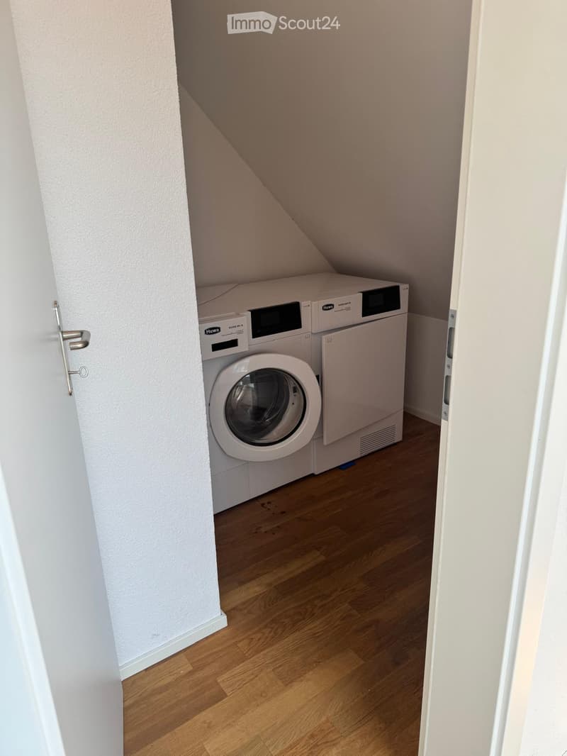 Small room with wooden flooring and white walls, featuring a washing machine and dryer unit.
