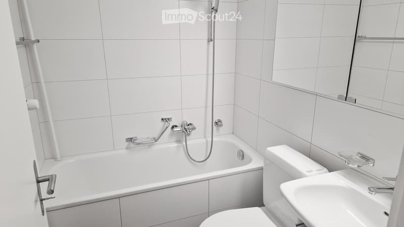 Modern bathroom with white tiles, bathtub, toilet, sink, and mirror.