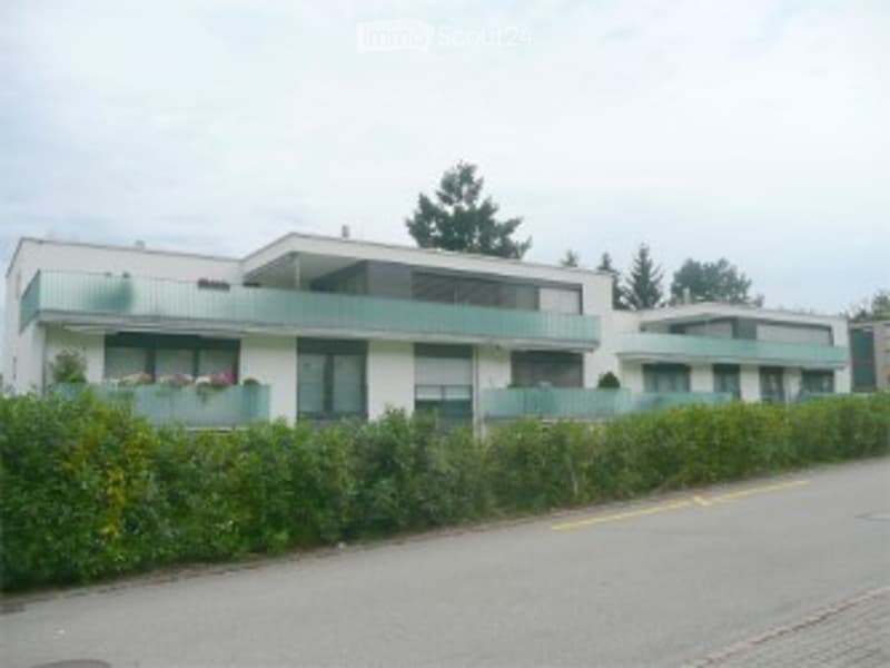Modern multi-story residential building with balconies, large windows, and surrounding greenery.