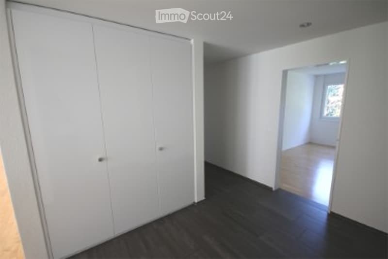 Empty room with dark wooden flooring, white walls, and a large built-in wardrobe. The adjacent room is also empty with wooden flooring and white walls.