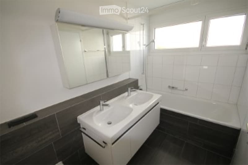 Modern bathroom with white tiles, dark wood accents, a large mirror, a sink with a modern faucet, and a bathtub.