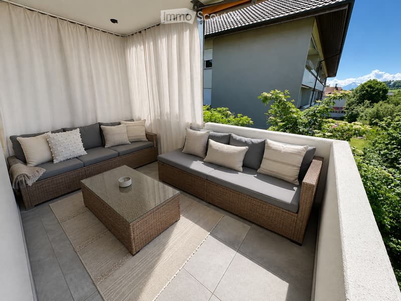 Balcony with two wicker sofas, cushions, coffee table, and curtains, overlooking a green garden.