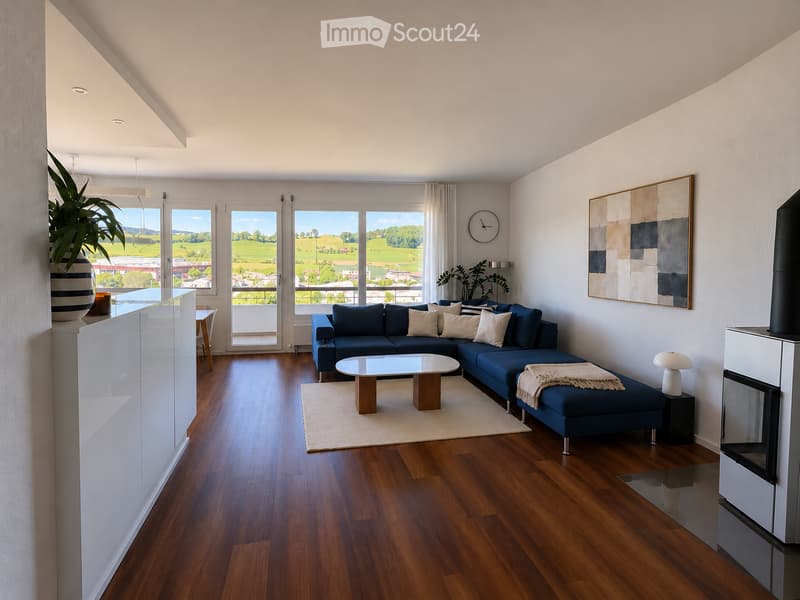 Modern living room with wooden flooring, large windows offering a scenic view, a blue sectional sofa, a glass coffee table, a fireplace, and decorative artwork.