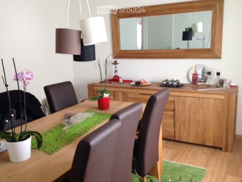 Dining room with a wooden dining table surrounded by grey upholstered chairs, a wooden cabinet with decorative items, a large mirror on the wall, and potted plants on the table and floor.