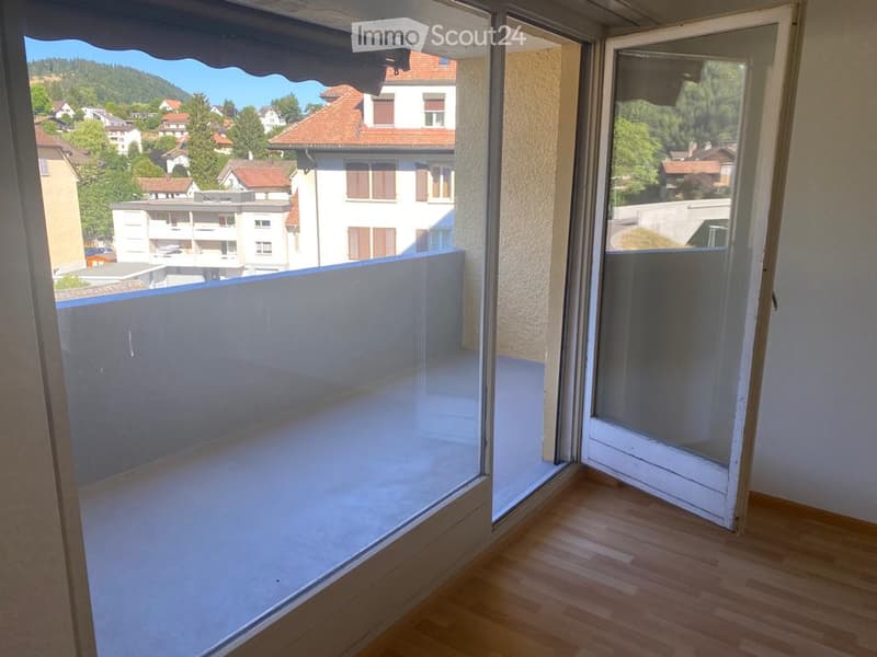Balcony with wooden flooring, large glass sliding doors, and scenic view of surrounding houses and greenery.