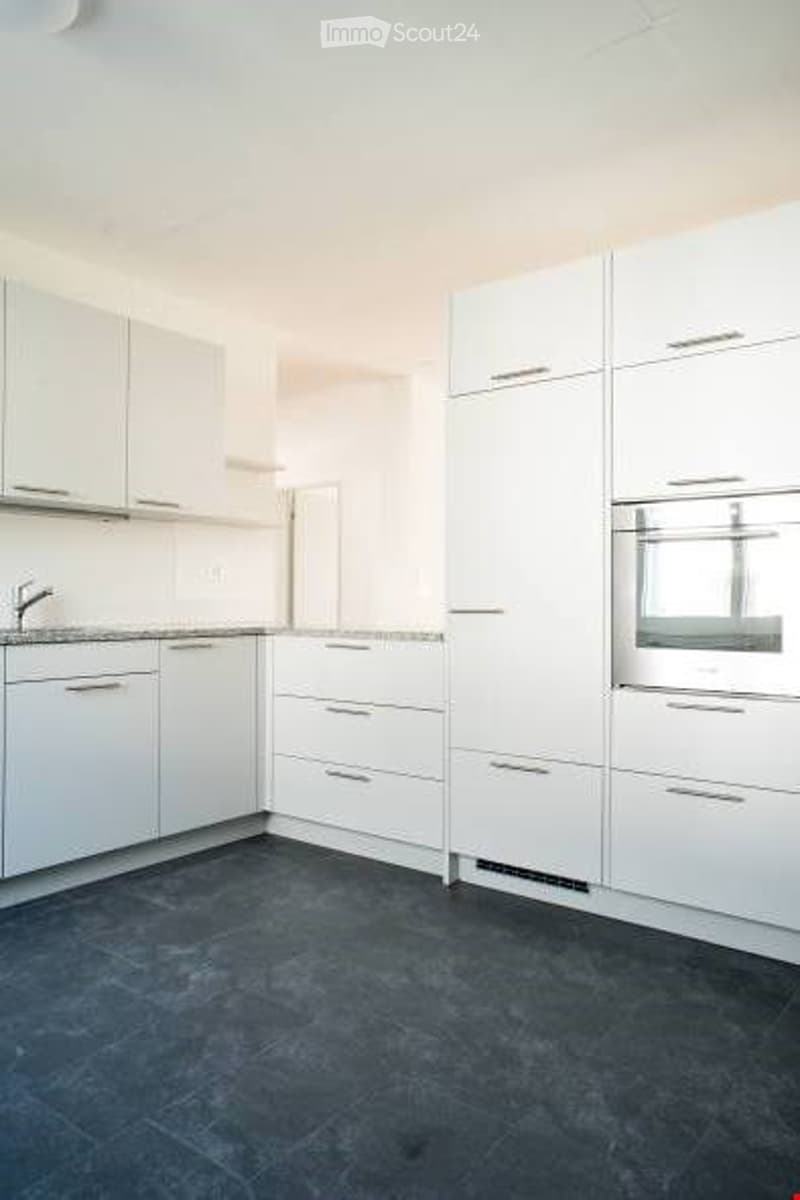 Modern kitchen with white cabinets, granite countertops, and a built-in oven. The floor is dark grey tiles.
