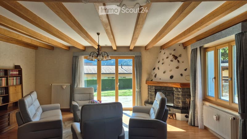 Cozy living room with exposed wooden beams, fireplace, large windows, and comfortable seating.