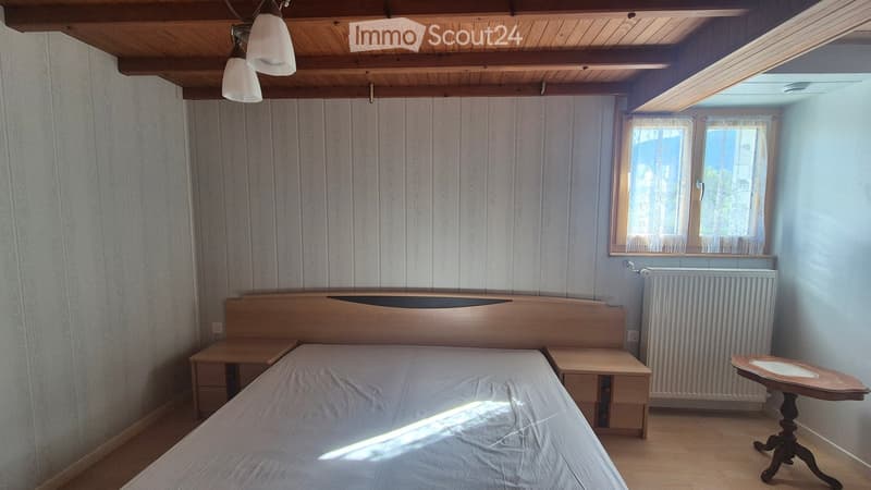 Cozy bedroom with wooden walls, a bed with a headboard, two nightstands, a radiator, and a small table near the window.