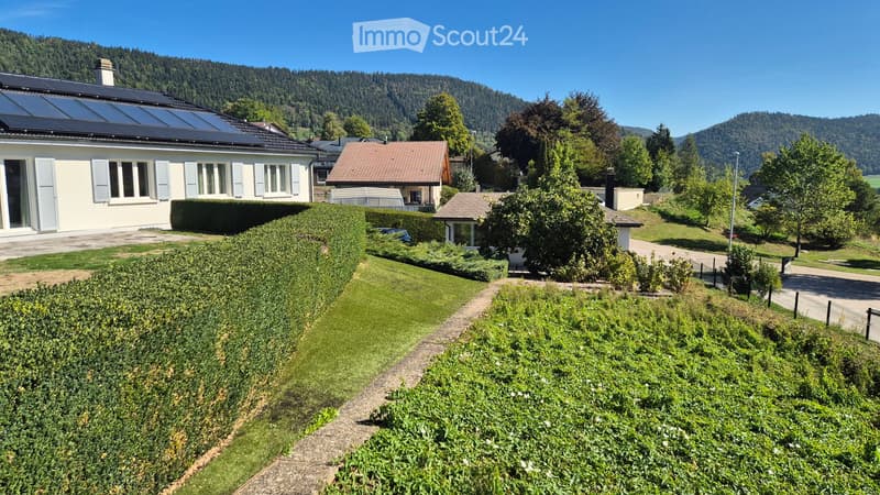 A peaceful residential area with multiple houses, well-maintained gardens, and a scenic mountain backdrop.
