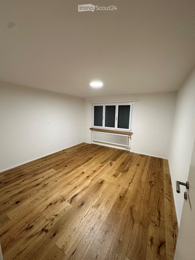 Empty room with wooden flooring, white walls, a window with blinds, and a radiator below it.