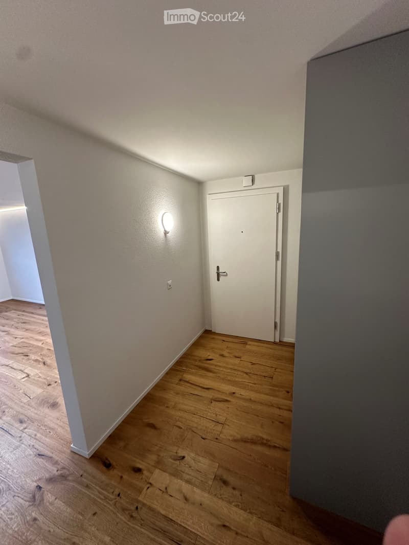 Empty hallway with wooden flooring, white walls, and a closed white door at the end.