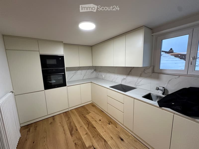 Modern kitchen with white cabinets, marble backsplash, wooden flooring, and stainless steel appliances including an oven, stove, and sink.