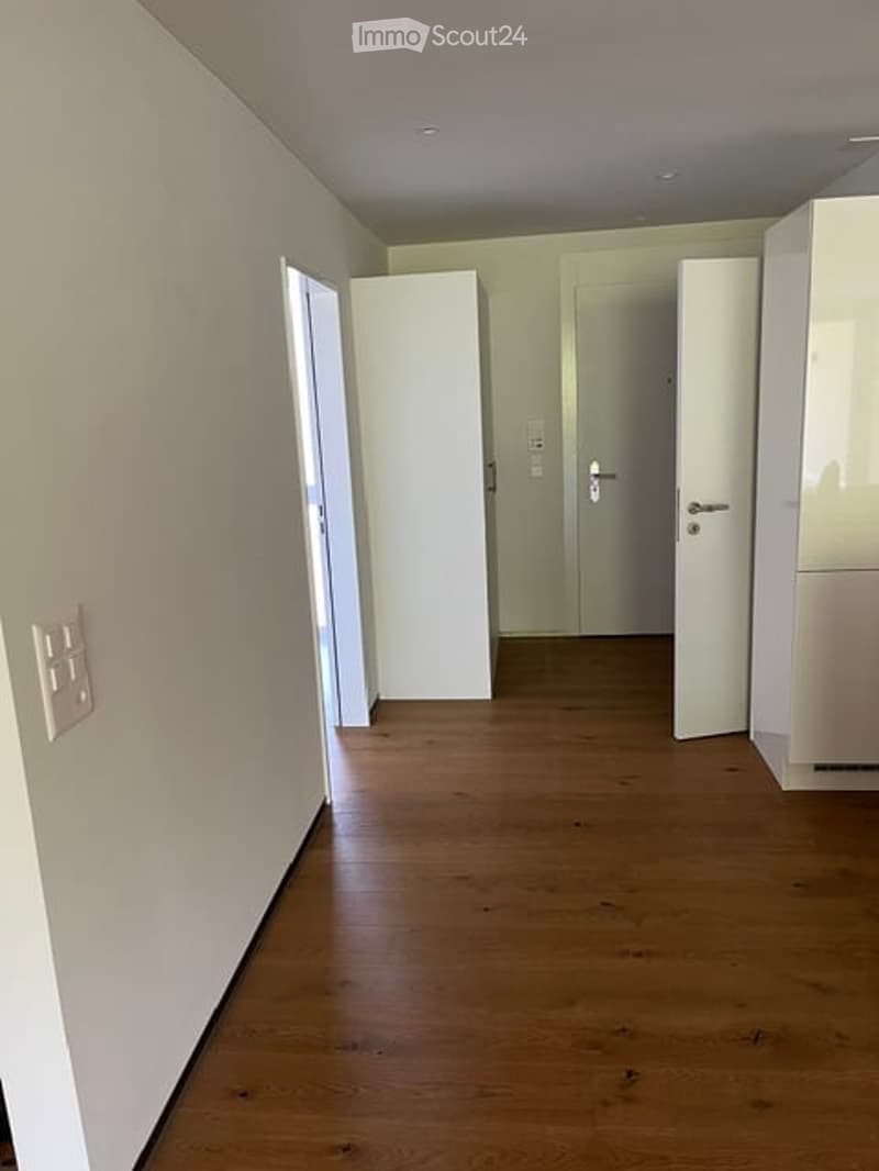 Empty hallway with wooden flooring, white walls, and several closed doors.