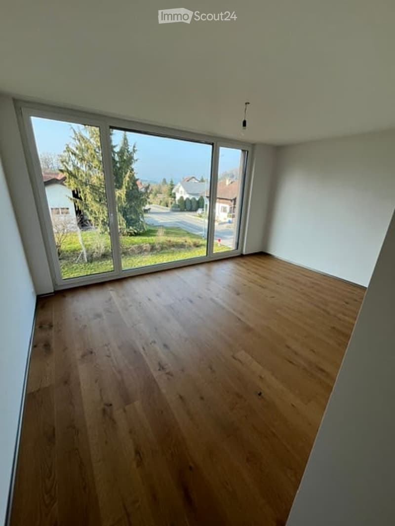 Empty room with wooden flooring and large windows offering a view of the outdoors.