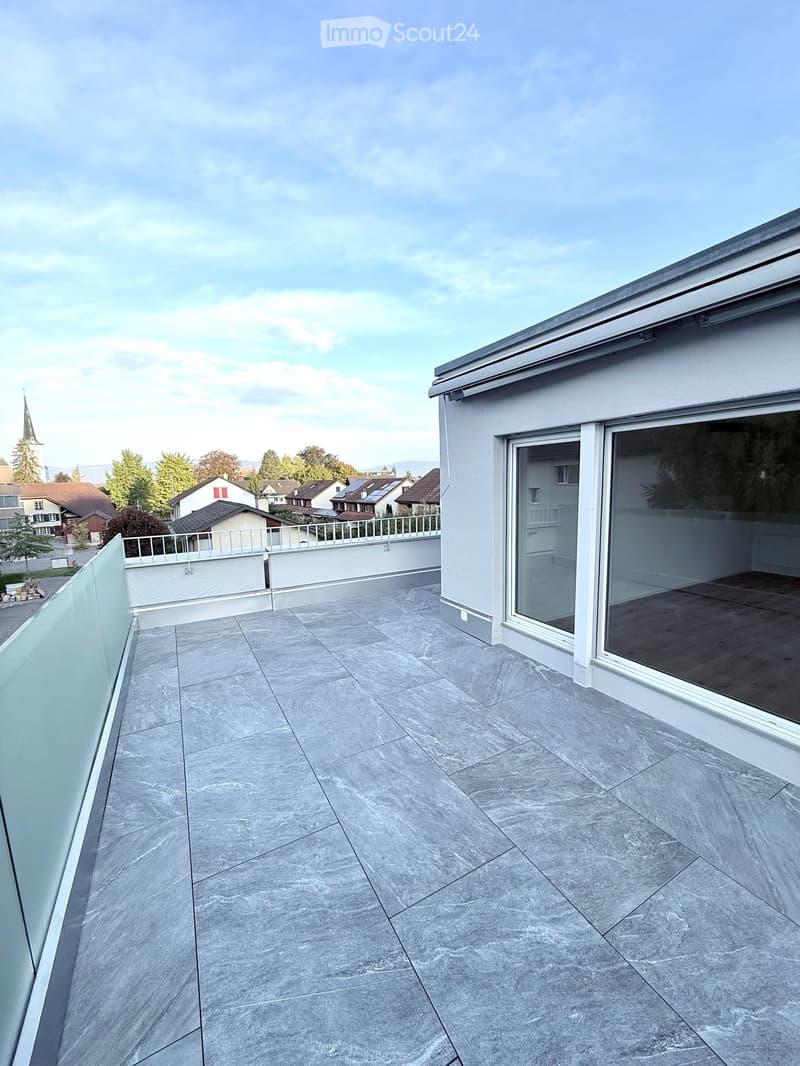 Modern balcony with grey stone tiles, glass railing, and open view of the neighborhood.