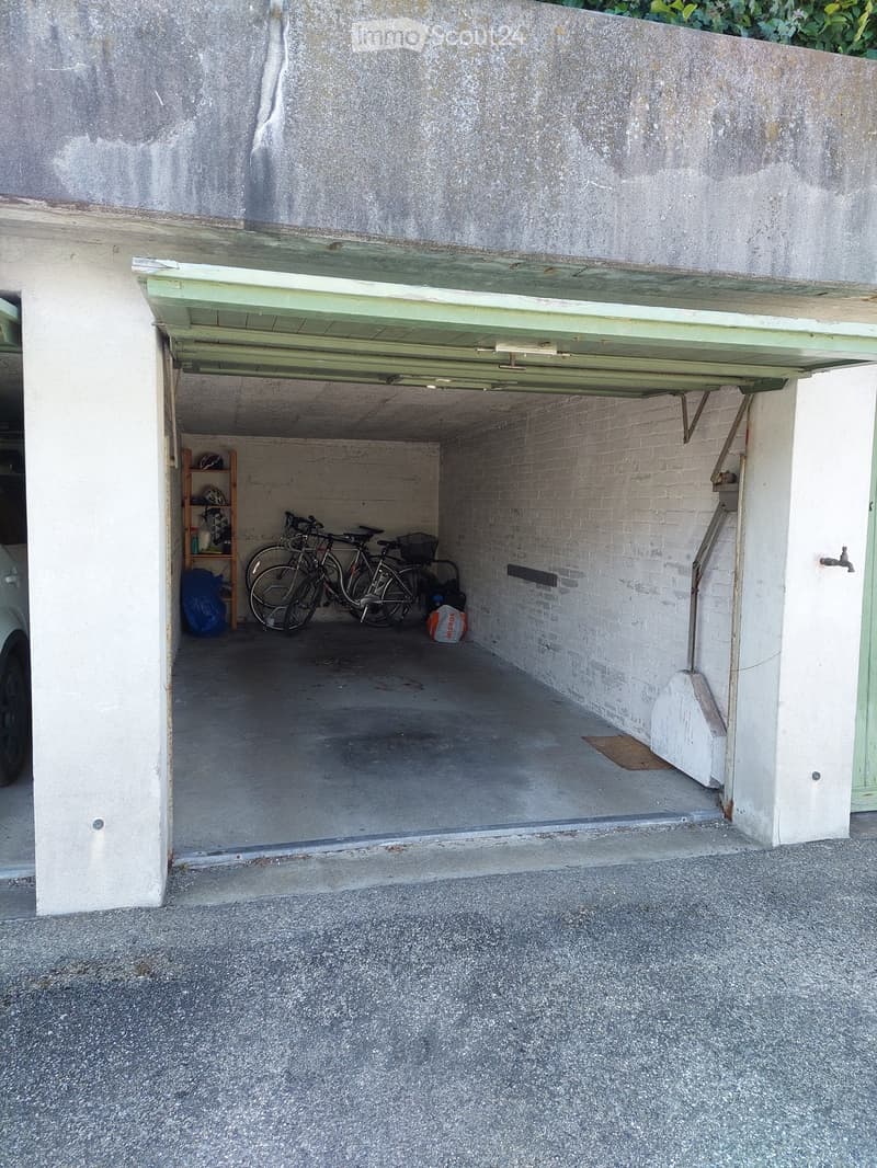 Underground garage with concrete floor, white brick walls, bicycles, and a small shelf with items.