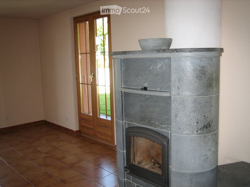 A room with a stone fireplace, a bowl on top, and a wooden door leading outside.