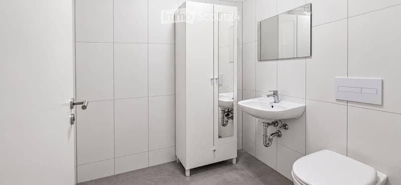 Modern bathroom with white tiles, a sink, a mirror, a cabinet, and a toilet.