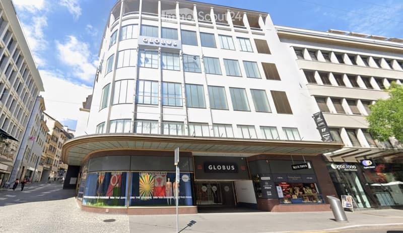 Modern multi-story building with large windows and a curved facade, featuring commercial storefronts at the ground level with signage for 'Globus' and other businesses.