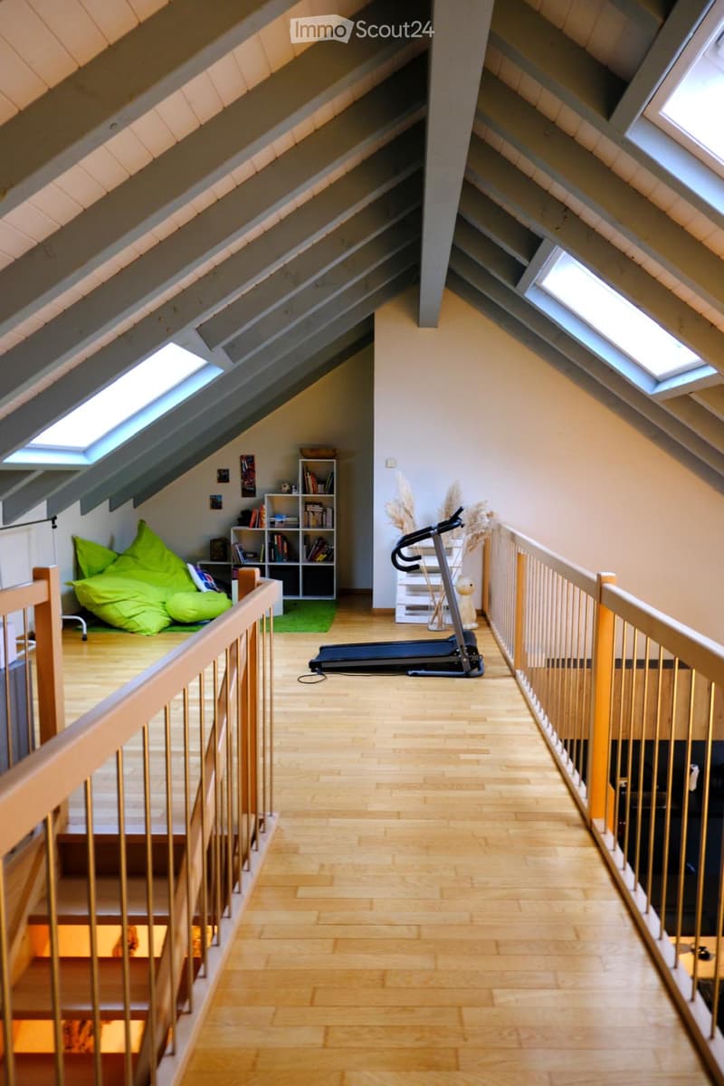 Loft-style room with wooden flooring, exposed wooden beams, skylights, a green bean bag chair, a bookshelf, and a treadmill.