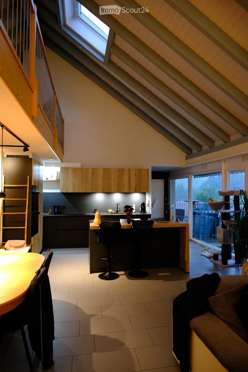 Open-plan living and dining area with a modern kitchen, featuring a sofa, dining table, chairs, kitchen island, and a cat tree in the corner.