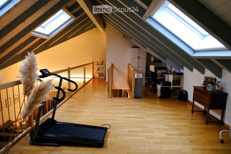 Spacious attic room with wooden flooring, skylights, a treadmill, a desk area with a chair, and a small cabinet.