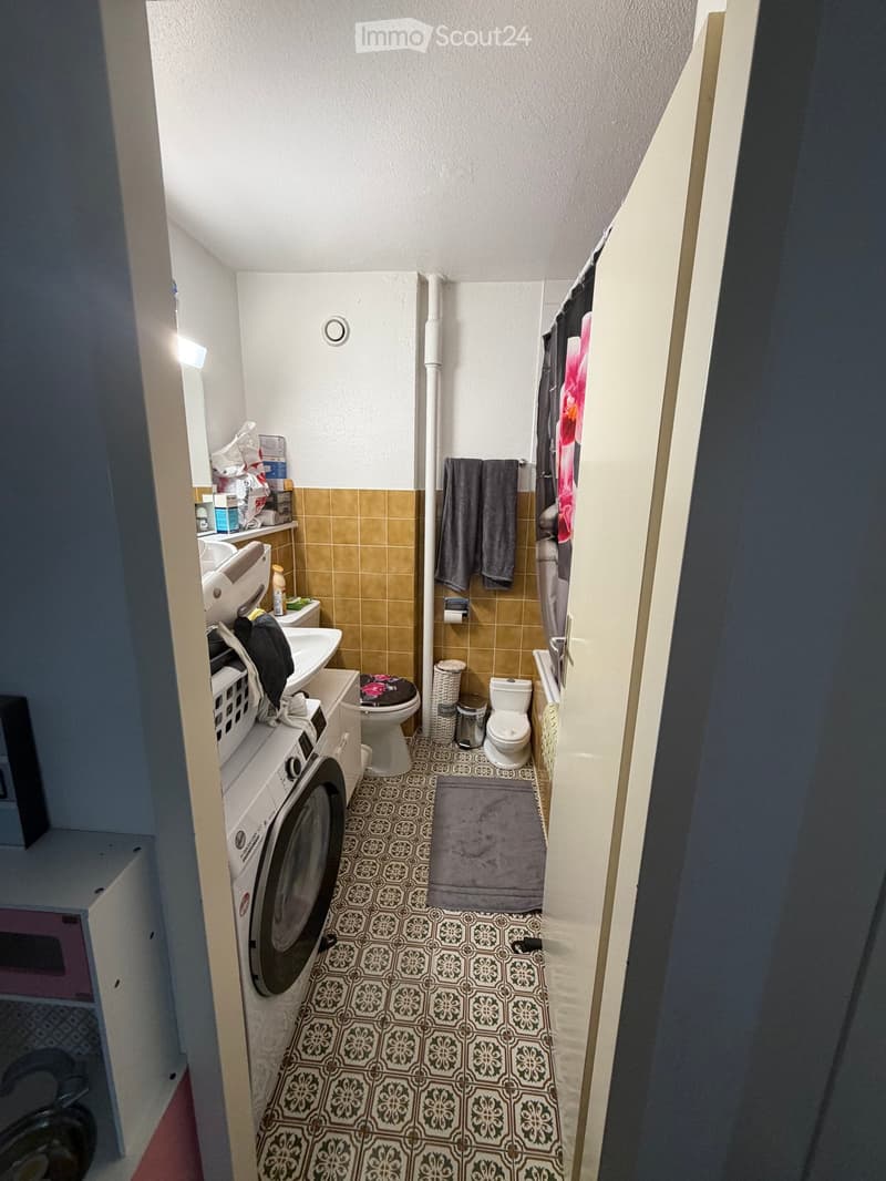 Small bathroom with a washing machine, toilet, sink, towels, and a shower curtain.
