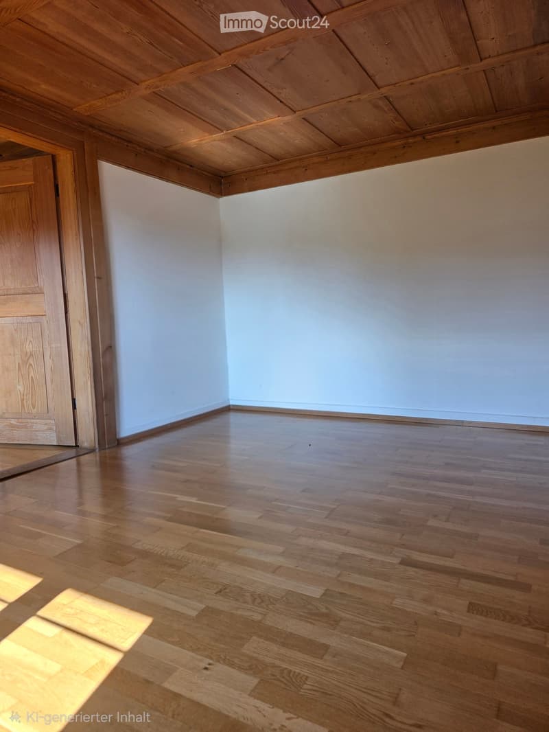 Empty room with light wooden flooring and white walls, featuring a wooden door frame and a slanted wooden ceiling.