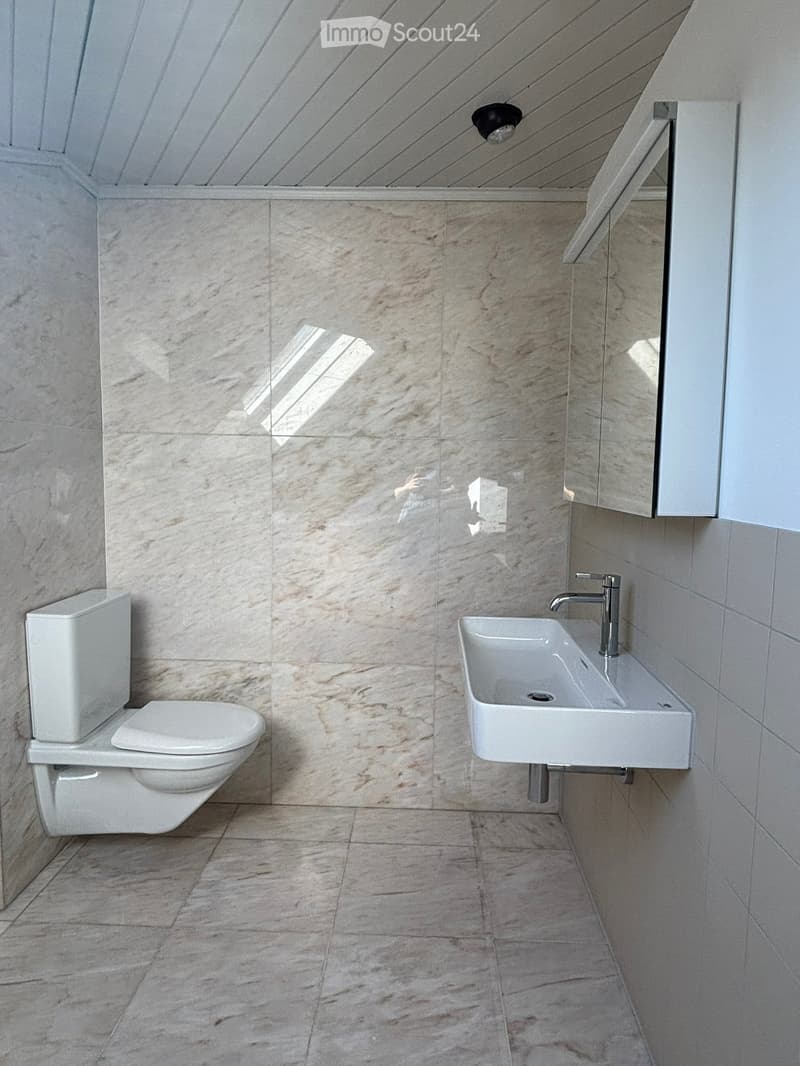 Modern bathroom with marble tiles, white toilet, wall-mounted sink, and sleek faucet.
