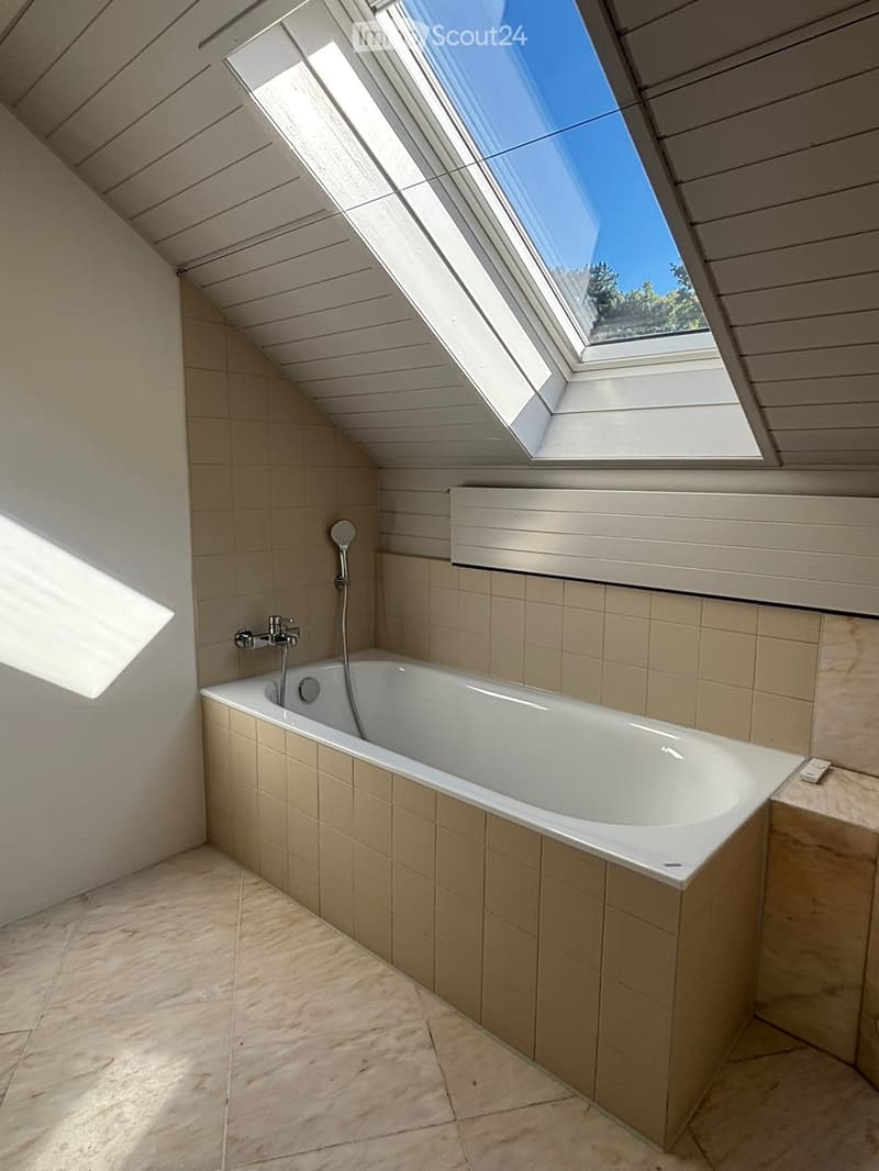 Modern bathroom with a large skylight, bathtub, and tiled walls and floor.
