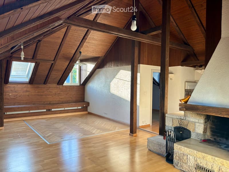 Spacious living room with exposed wooden beams, wooden flooring, large windows, and a stone fireplace.