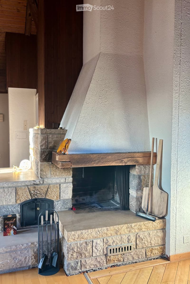Stone fireplace with wooden mantel, fireplace tools, and wooden floor.
