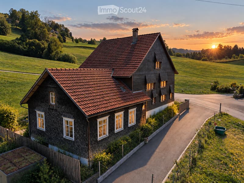 A two-story wooden house with a red-tiled roof, surrounded by a lush green landscape and a winding road.