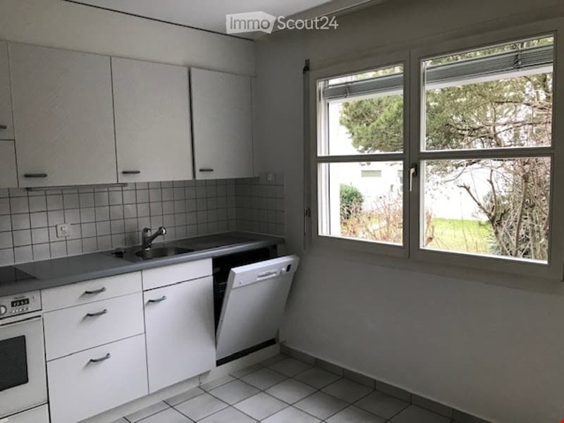 Modern kitchen with white cabinets, a sink, a dishwasher, and an oven. The space features tiled walls and a tiled floor, with large windows providing natural light.