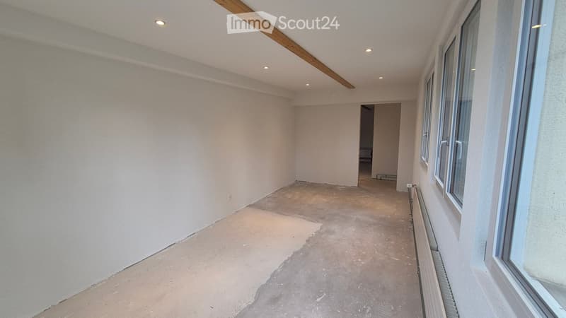 Empty room with white walls, concrete floor, and large windows. No furniture or equipment present.