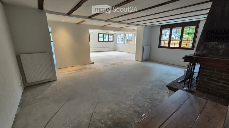 Empty room with exposed wooden beams on the ceiling, concrete floor, and large windows. No furniture or equipment present.