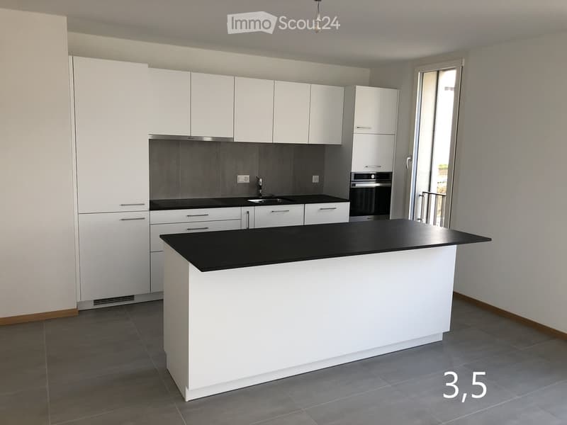 Modern kitchen with white cabinets, black countertops, and a central island. Features a sink, oven, and ample storage space.