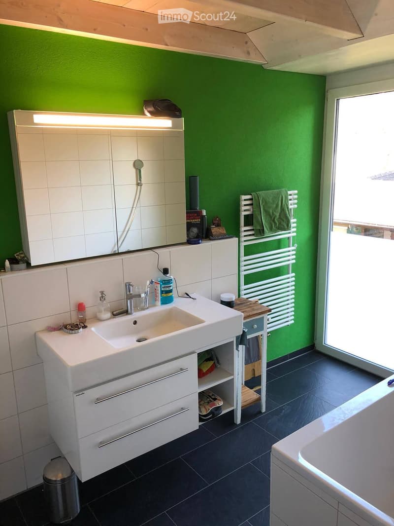 Modern bathroom with green walls, white sink, mirror, radiator, and bathtub.