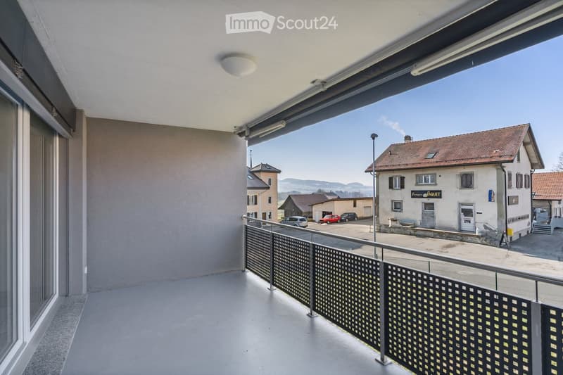 Balcony with metal railing, overlooking a town with buildings, parked cars, and a clear sky.