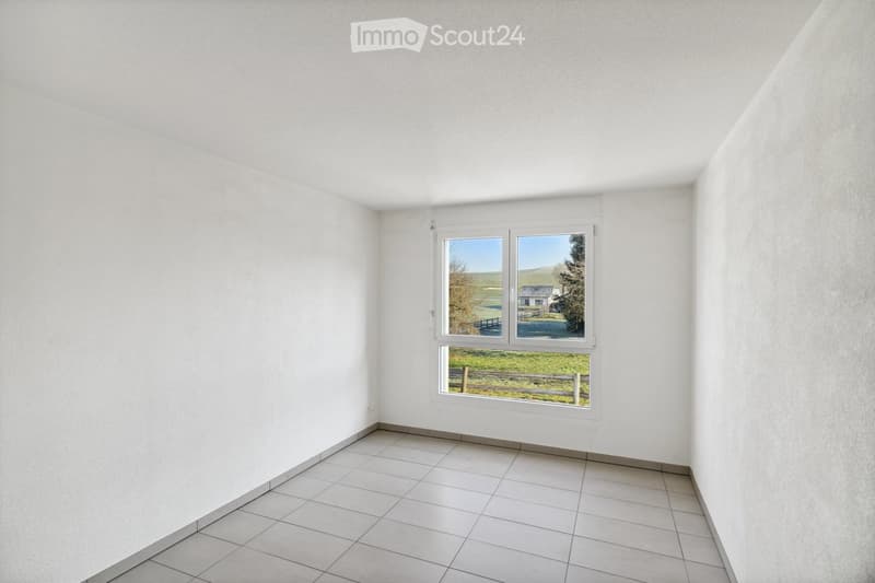 Empty room with white walls, tiled floor, and large windows overlooking a rural landscape.