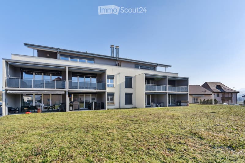 Modern two-story house with large windows, balconies, and a spacious lawn in front.