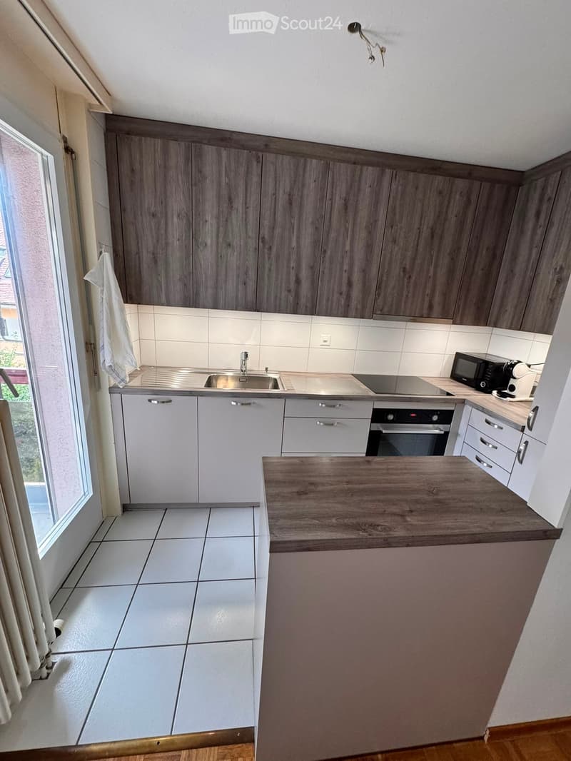 Modern kitchen with grey and white cabinets, stainless steel sink, microwave, oven, coffee maker, and a wooden countertop.