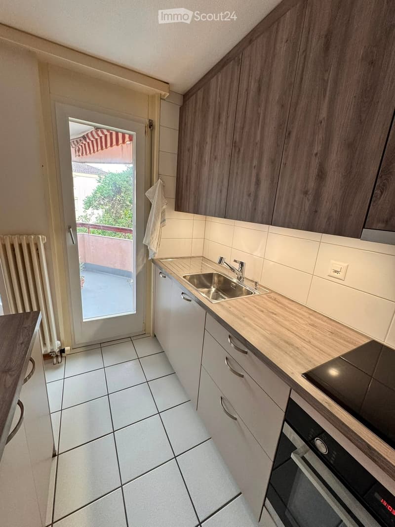 Modern kitchen with white cabinets, a stainless steel sink, and a built-in oven. The space features tiled flooring and a door leading to a balcony or terrace.