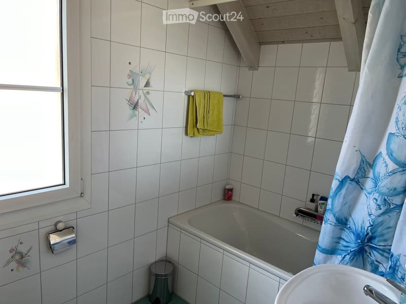 Bathroom with white tiled walls, a bathtub, a towel rack with a yellow towel, a shower curtain, a toilet paper holder, a sink, and a small trash can.