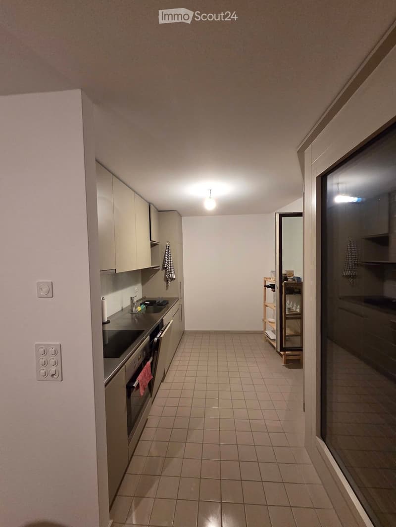 Modern kitchen with tiled floor, white cabinets, stainless steel sink, oven, and a small wooden shelf near the entrance.