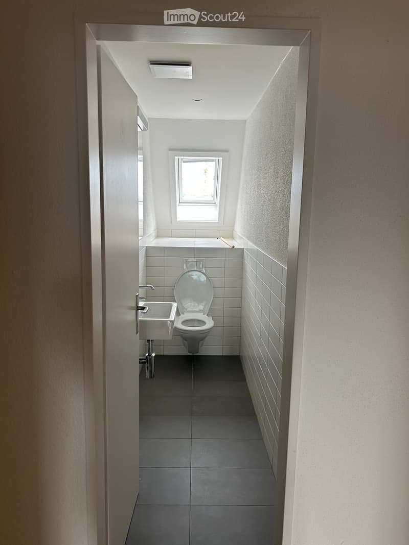 Modern, minimalist bathroom with a toilet, sink, and faucet, featuring grey tiles and white walls.