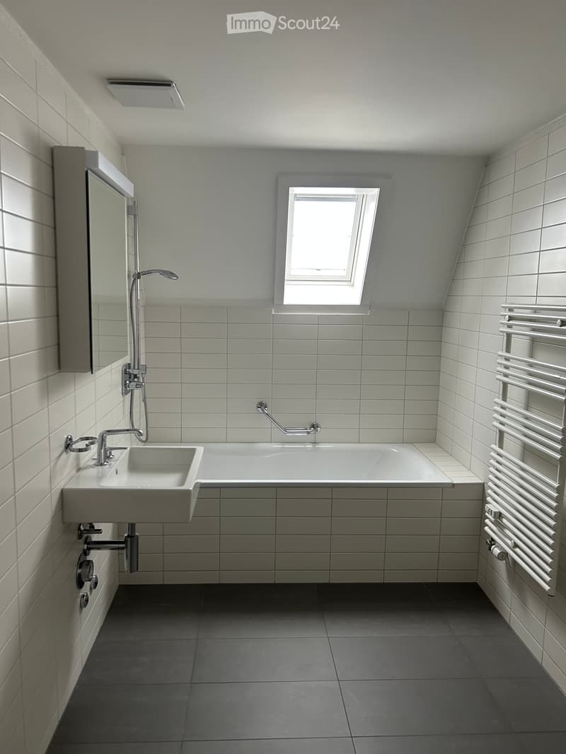 Modern bathroom with white tiles, a large window, a sink, a bathtub, a mirror, and a radiator.